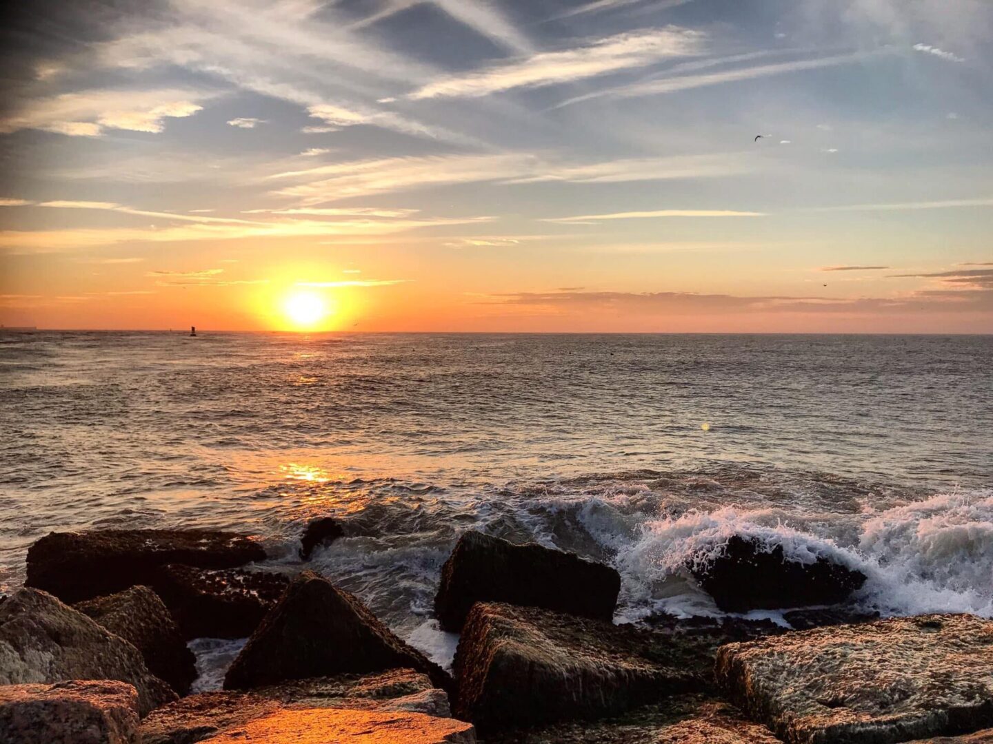 A sunset over the ocean with rocks in front of it.