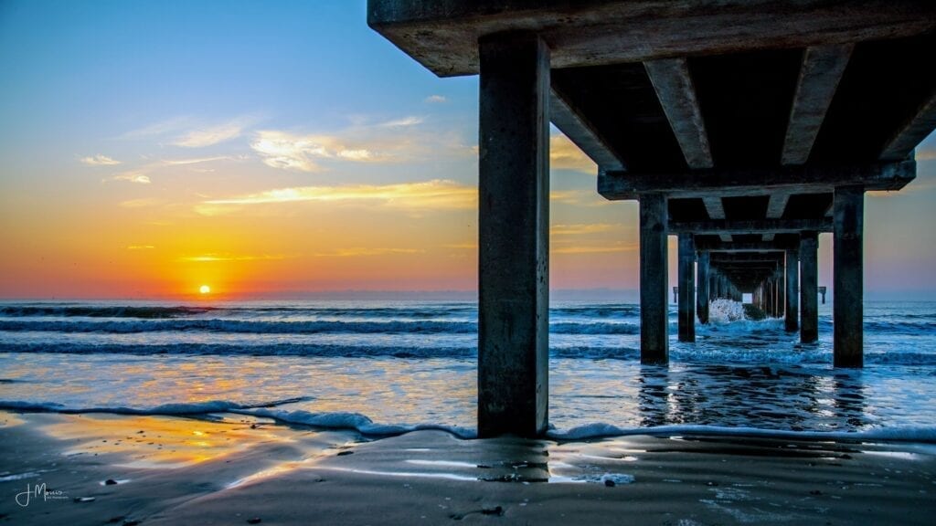 A pier with the sun setting over the ocean.