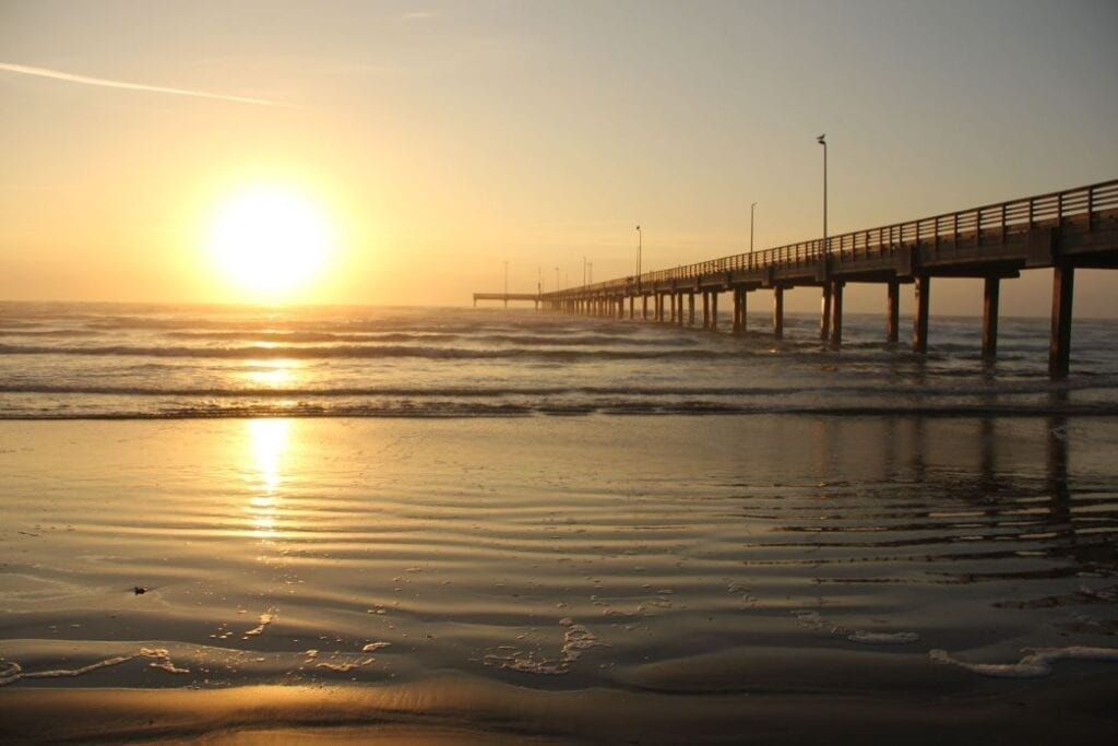 A pier with the sun setting over the ocean.