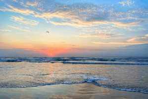 A sunset over the ocean with waves crashing on it.