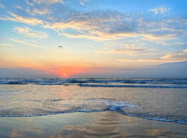 A sunset over the ocean with waves crashing on it.