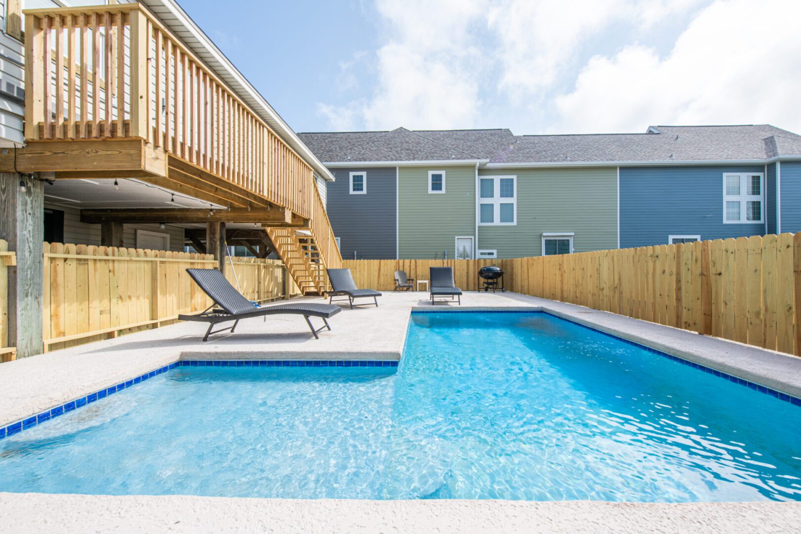 A pool with two chairs and a deck in the background.