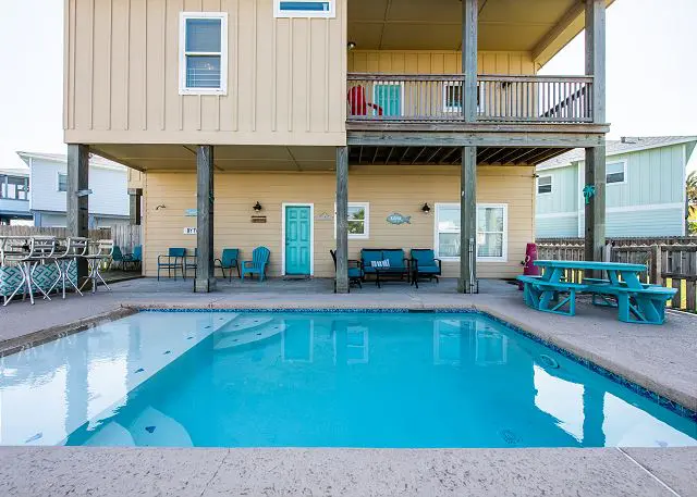 A pool in front of a house with a deck.