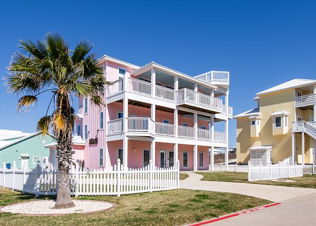 A pink building with white balconies and palm tree.
