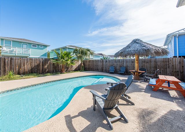 Sunny backyard with a swimming pool and lounge chairs under a bright sky.