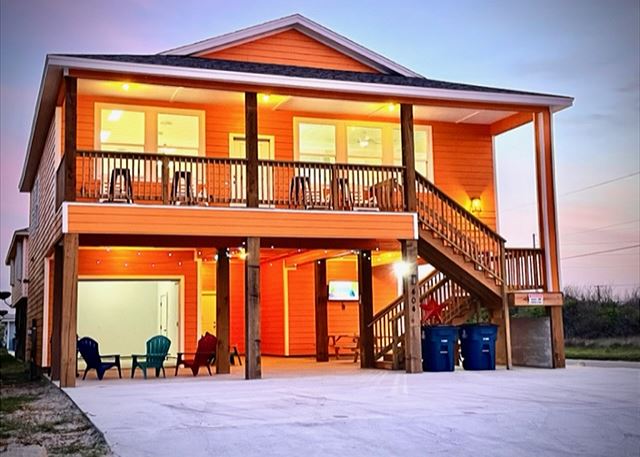 A warmly lit two-story house with outdoor stairs and seating area at dusk.