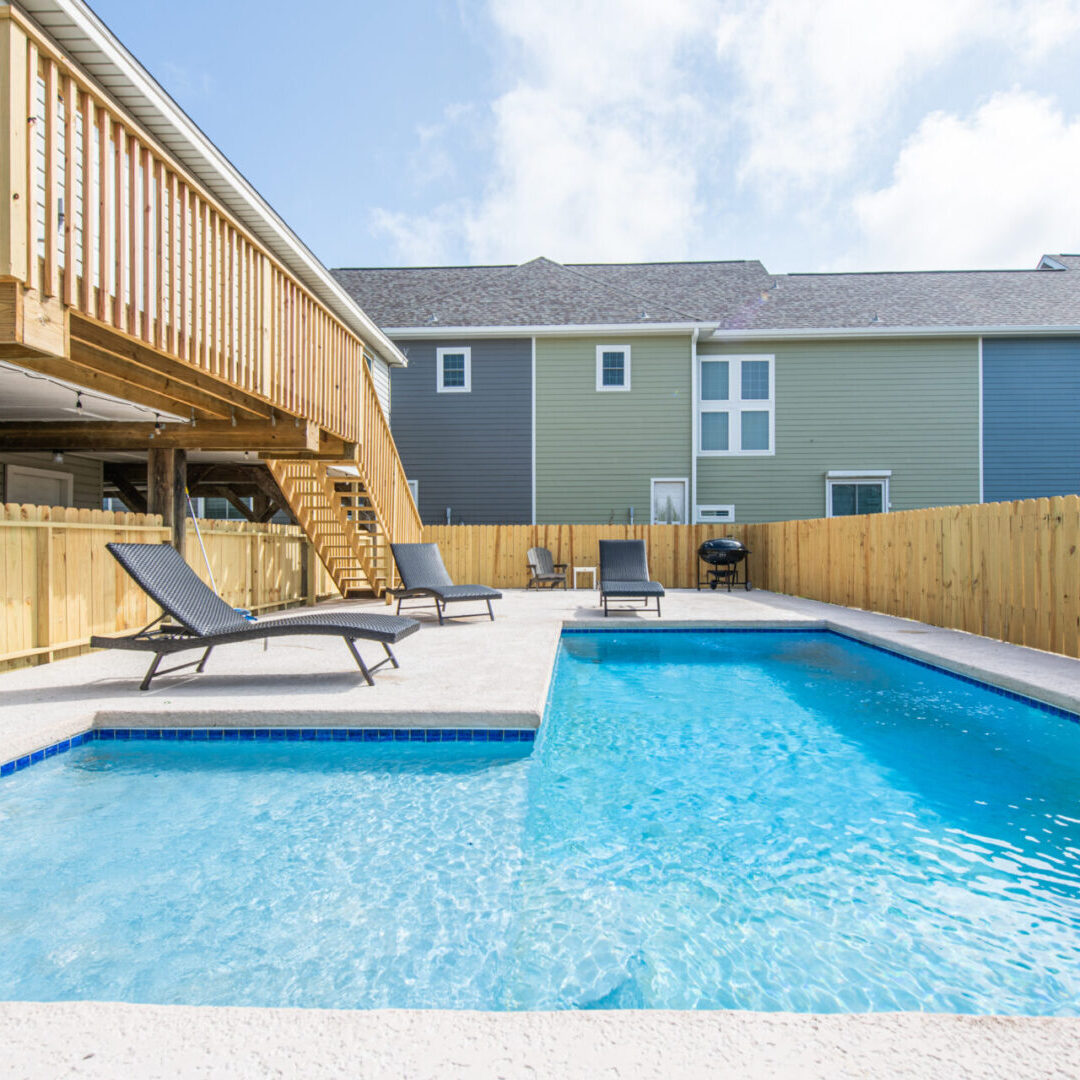 A pool with two chairs and a deck in the background.