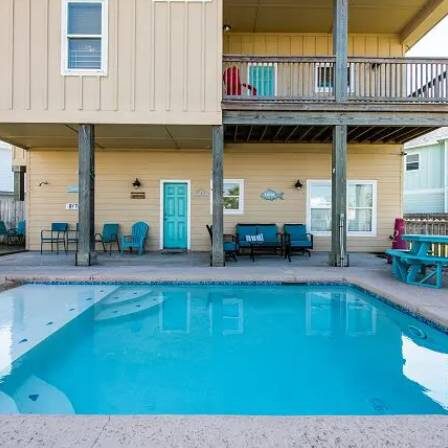 A pool with chairs and tables in the back yard.